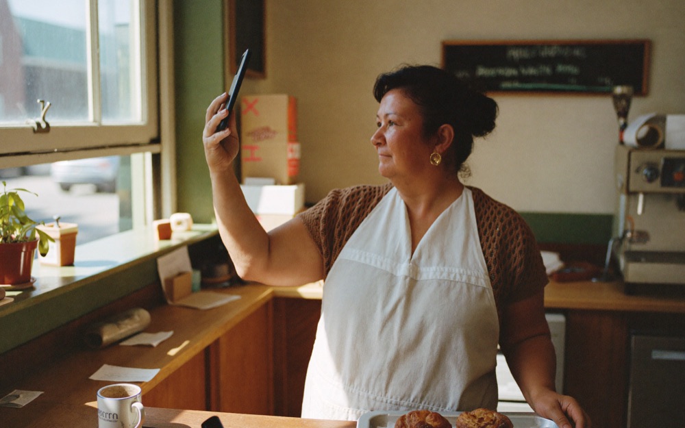 A bakery owner photographing a tray of pastries on her phone after closing