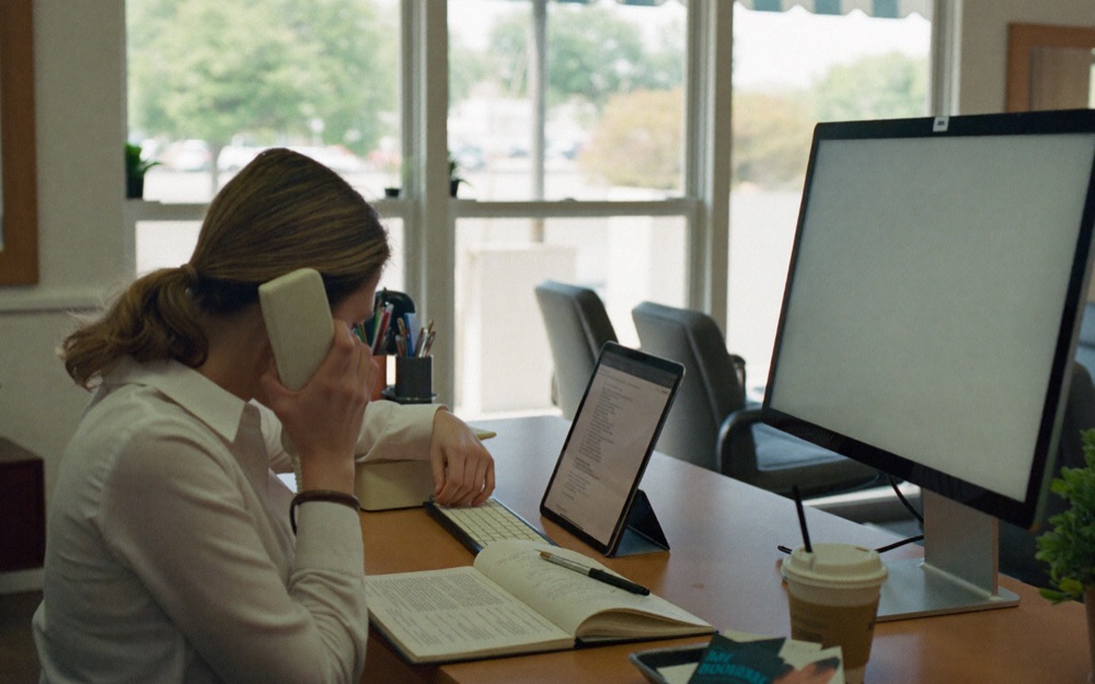 A salon receptionist on the phone with an appointment book and a tablet open in front of her