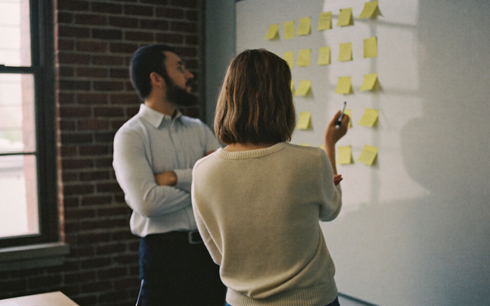 Two colleagues at a whiteboard covered in sticky notes